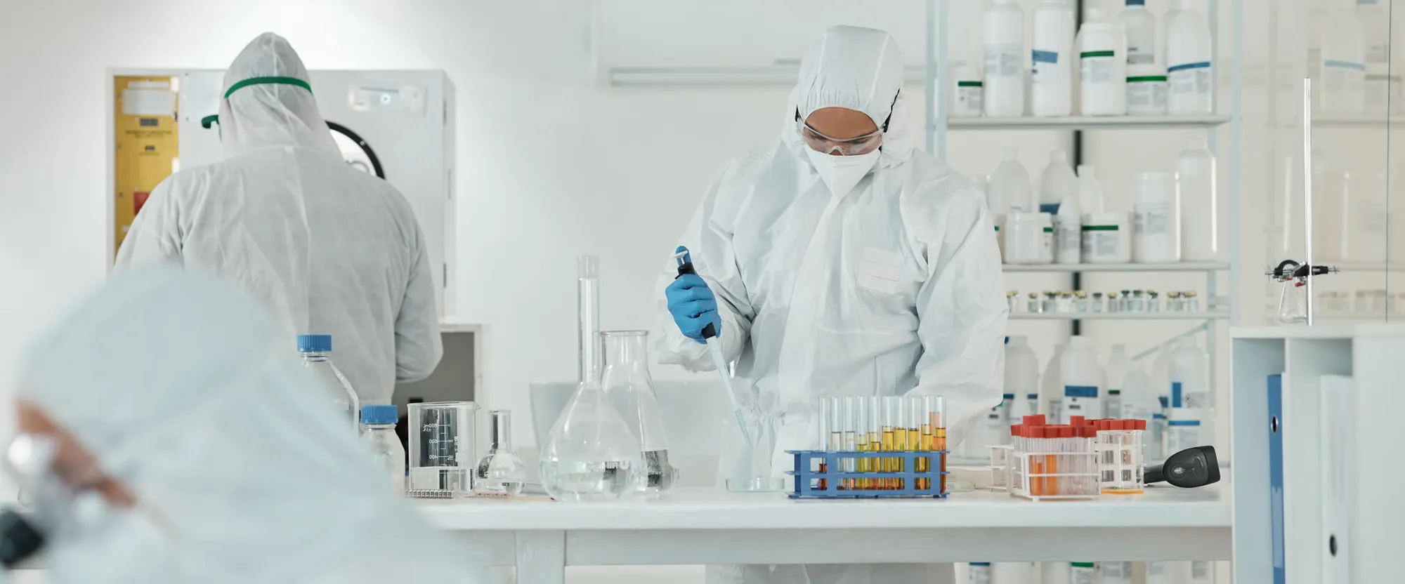 Técnico com macacão estéril, máscara e luvas pipetando amostras em sala limpa de laboratório