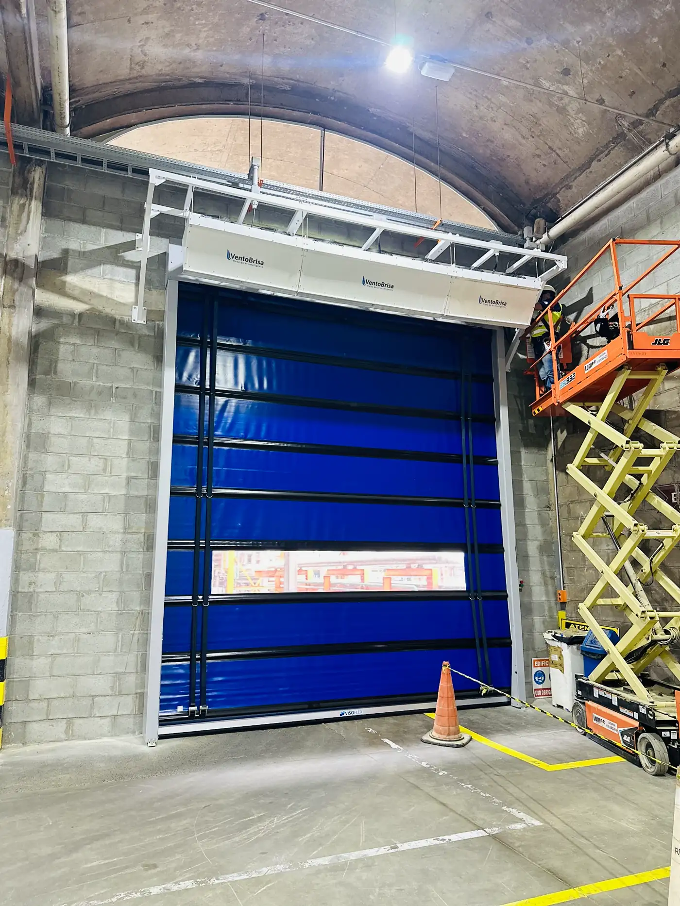 Cortinas de ar Visoflex instaladas acima de portas rápidas azuis de grande vão em galpão industrial