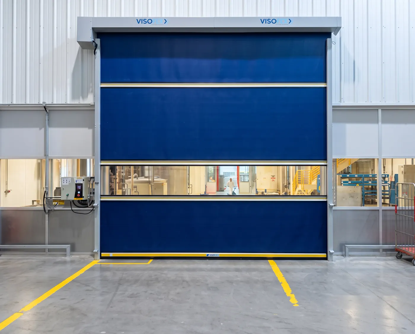 Porta rápida Visoflex VFX103 azul com visor em corredor de fábrica de alimentos, com área de produção ao fundo