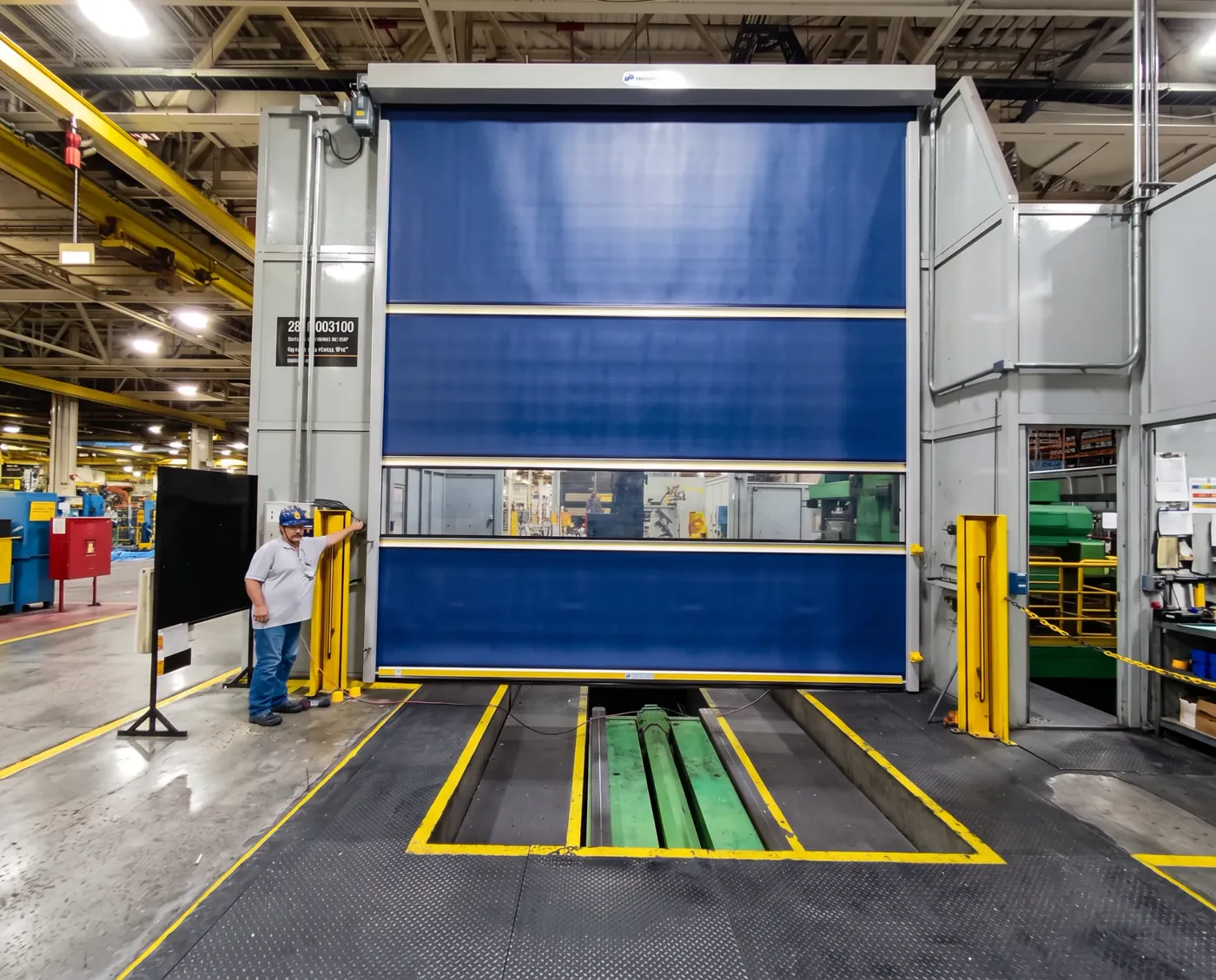 Porta rápida Visoflex VFX302 azul de grande porte em passagem de caminhões dentro de fábrica automotiva, com operador ao lado