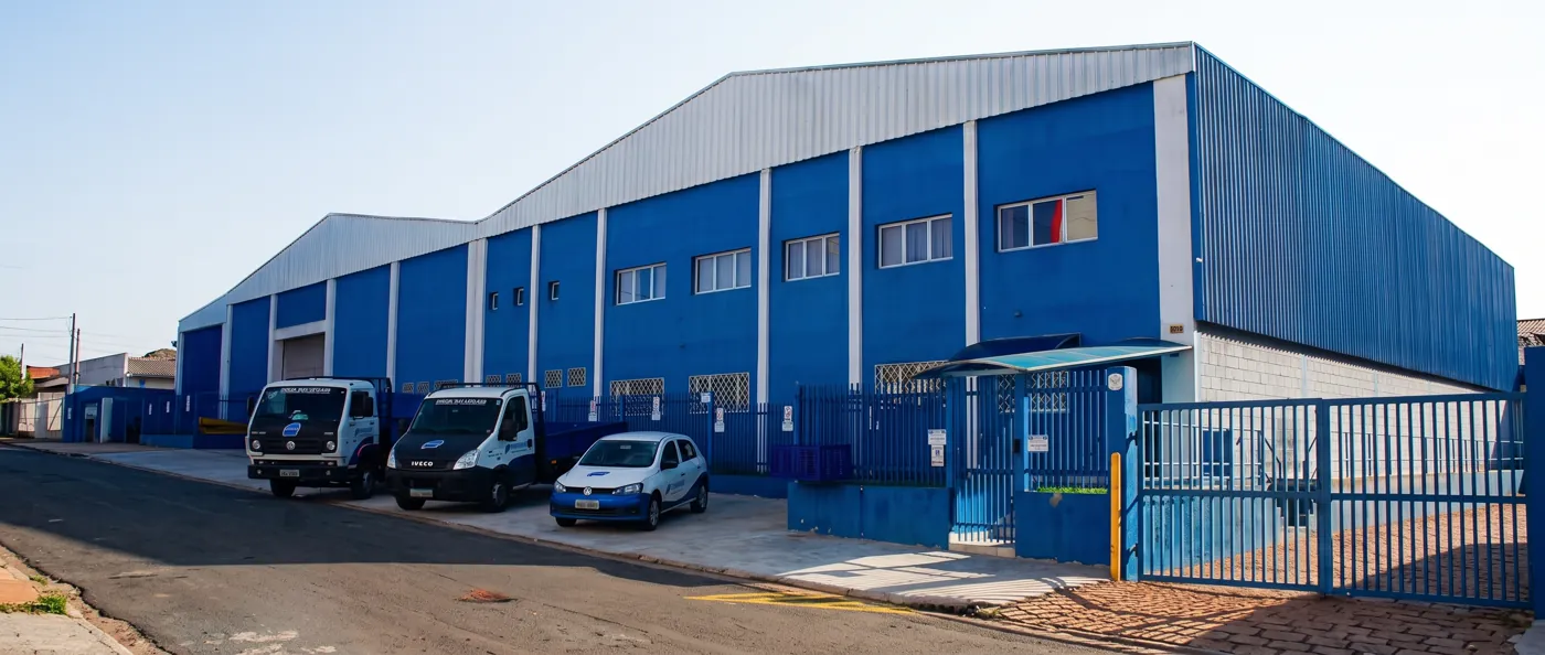 Fachada azul da fábrica da Visoflex em Indaiatuba/SP, com veículos da empresa estacionados em frente