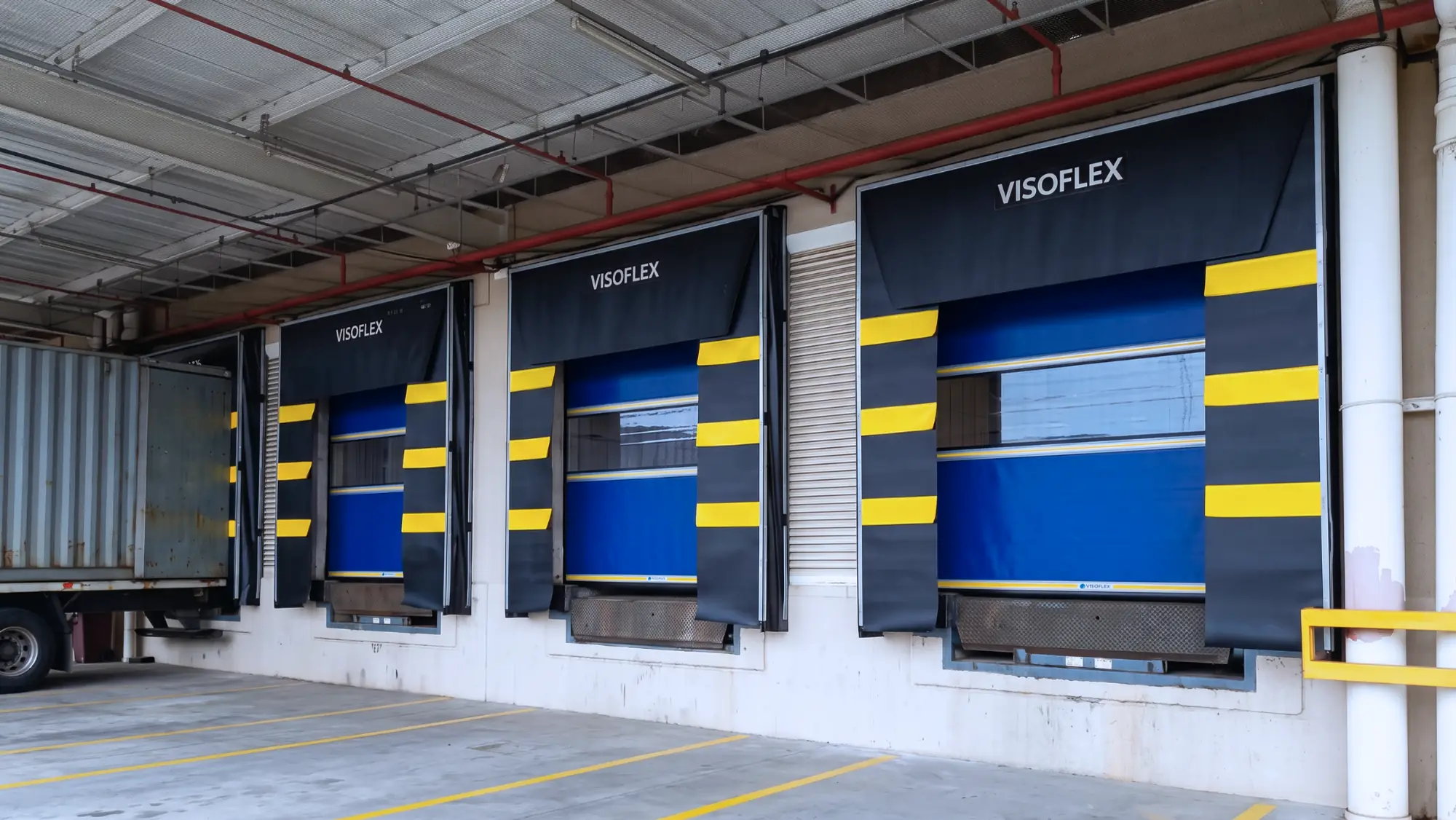Abrigos de doca Visoflex com faixas amarelas de orientação e portas de doca azuis em centro de distribuição