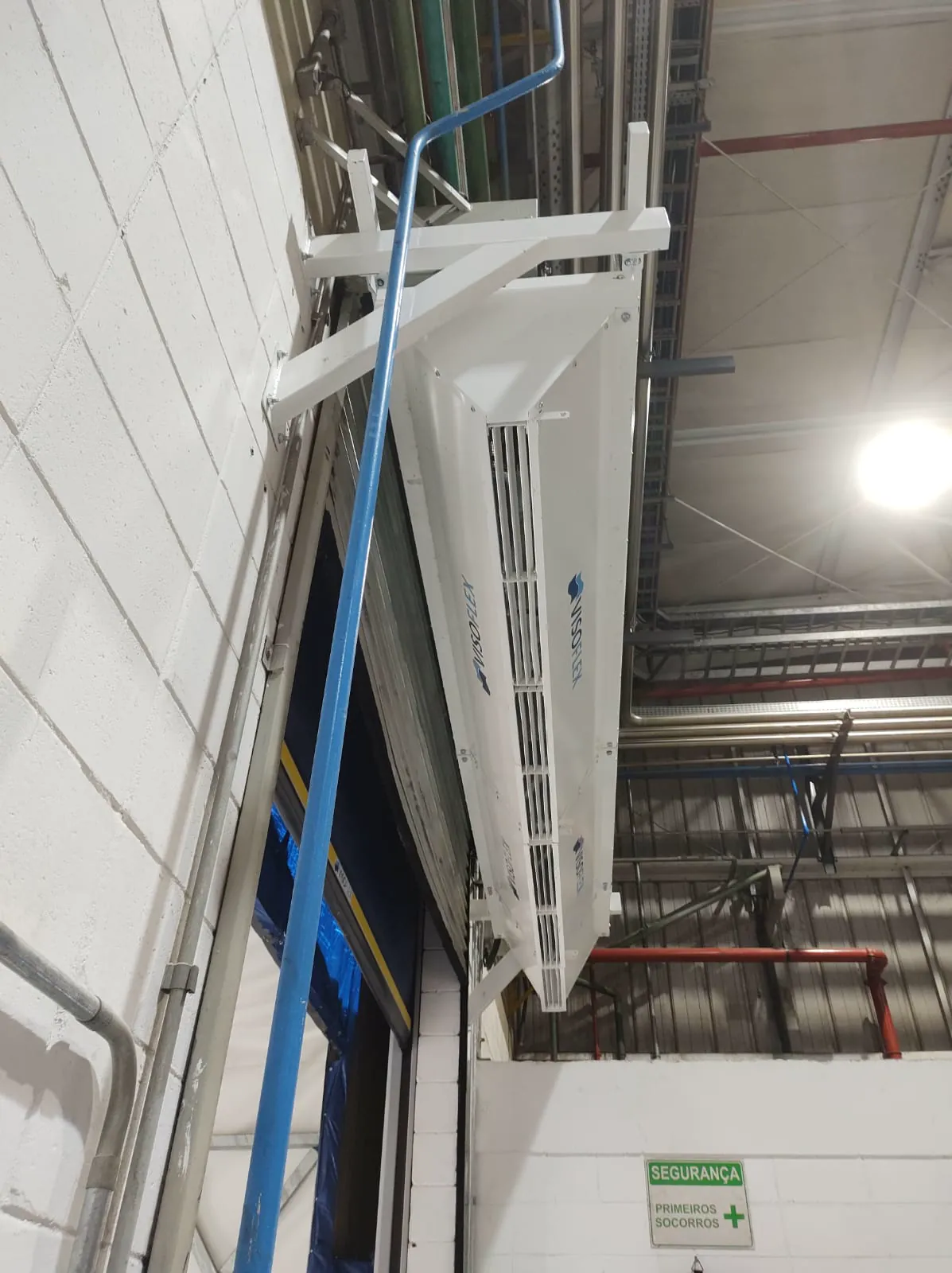 Cortina de ar Visoflex branca fixada com suportes metálicos acima de porta rápida, vista de baixo em área industrial