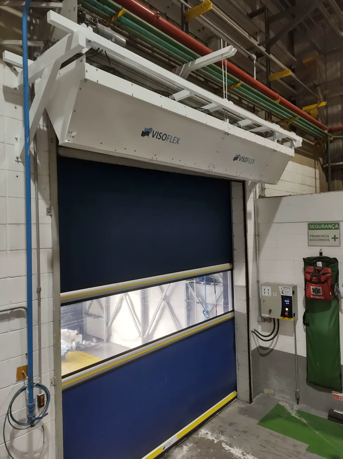 Cortina de ar Visoflex branca instalada com suportes sobre porta rápida em área industrial