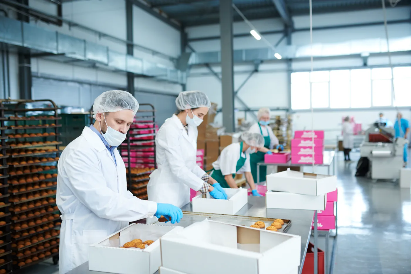 Operadores de touca, máscara e luvas embalando produtos em linha de indústria de alimentos