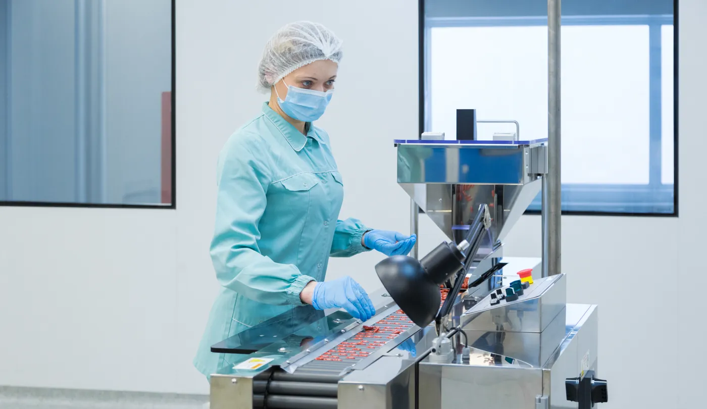 Operadora de touca e máscara trabalhando em máquina de indústria farmacêutica