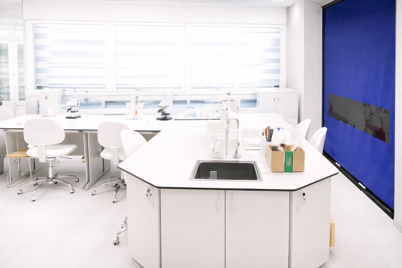 Laboratório branco com bancadas e porta rápida azul ao fundo