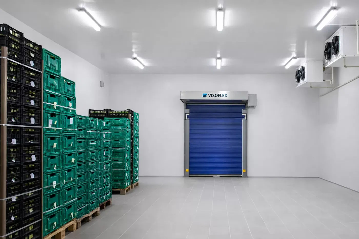 Câmara fria com caixas plásticas empilhadas e porta rápida azul Visoflex ao fundo